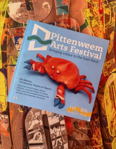 Pittenweem Arts Festival programme with a red crab cover displayed over colourful textile artwork