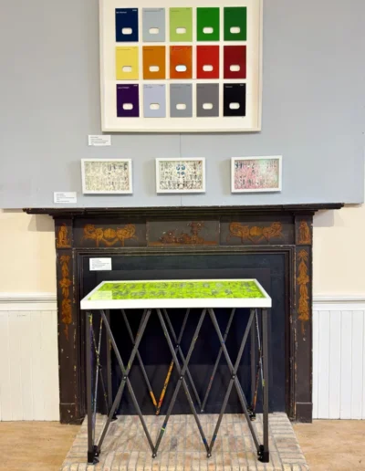 Shades of Menopause artwork displayed above a fireplace with smaller works
